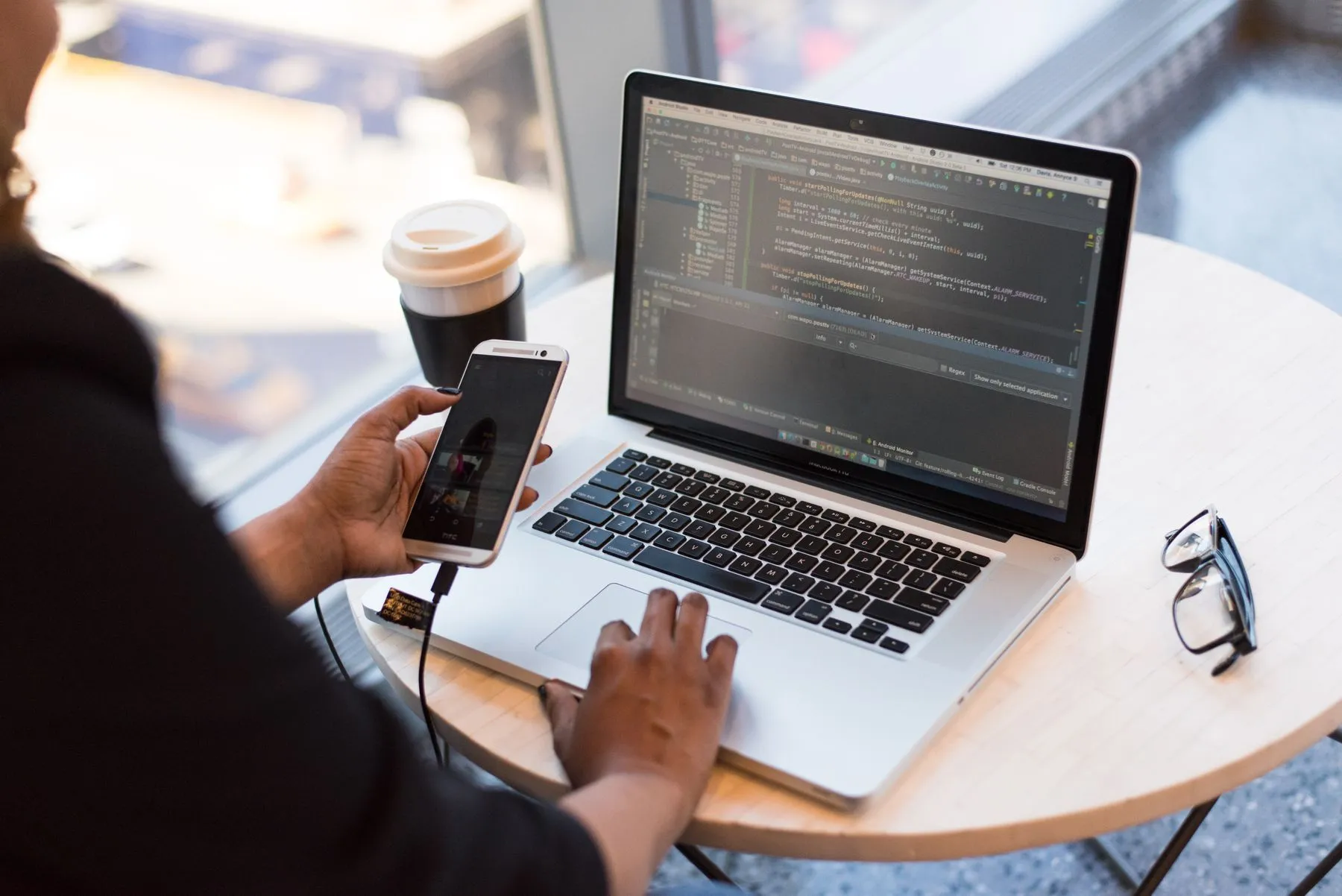 A developer holding a phone beside a laptop showing code